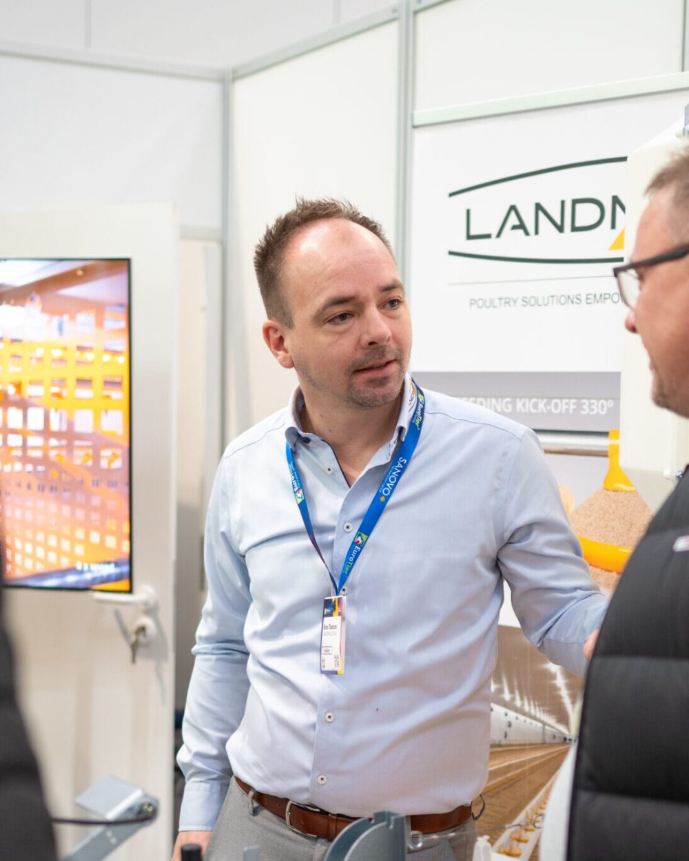 LANDMECO Sales Manager discussing poultry equipment with producers at a trade show.