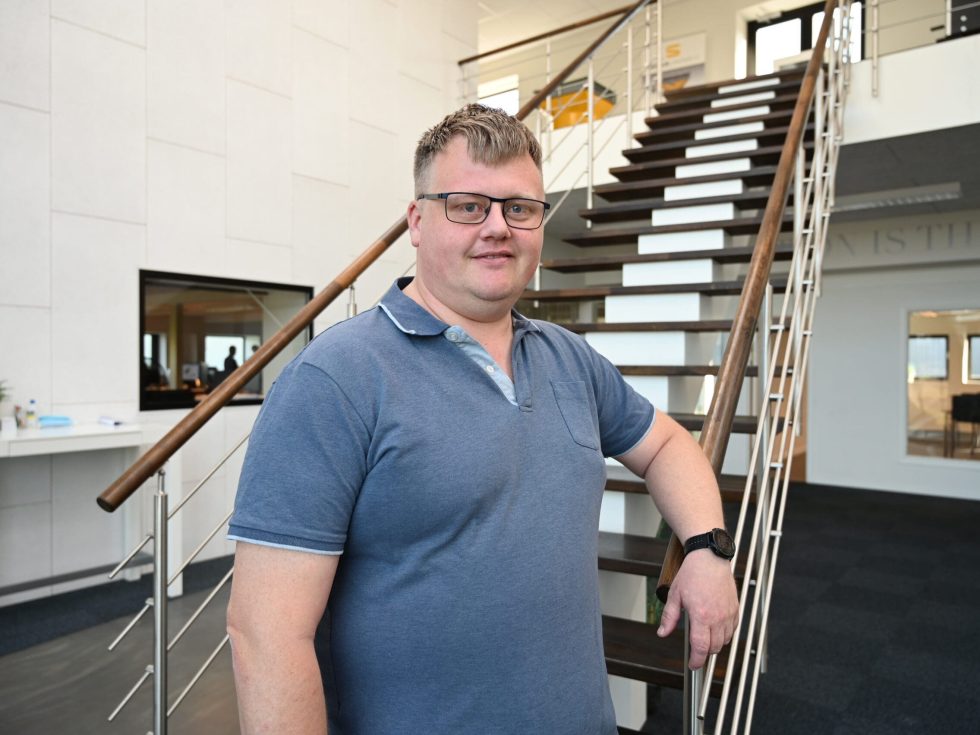 Morten Holm of LANDMECO standing by a staircase in the Ølgod office, wearing a blue polo shirt and glasses.