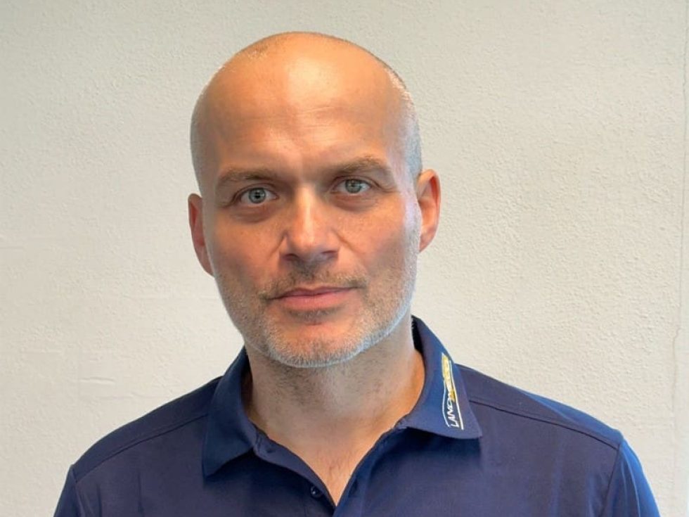 Tomasz Wróblewski from LANDMECO wearing a blue branded polo shirt, representing Scandinavian poultry equipment solutions.