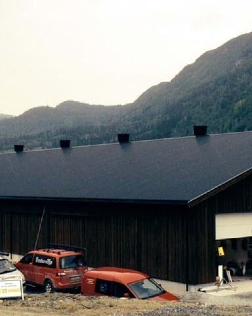 Modern dark wood poultry house with roof vents in a mountainous landscape, showcasing LANDMECO equipment.