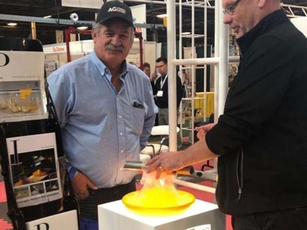 LANDMECO representatives demonstrating a yellow poultry pan feeding system at a trade show booth.