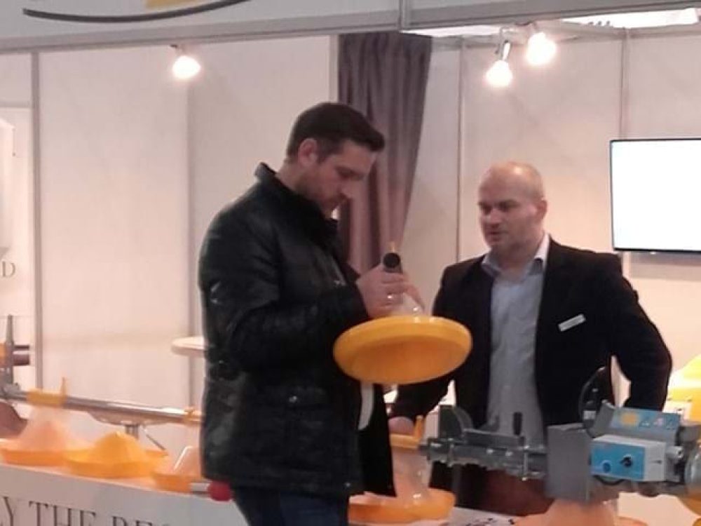 Professionals at LANDMECO Ferma Exhibition booth examining a yellow broiler pan feeding system.