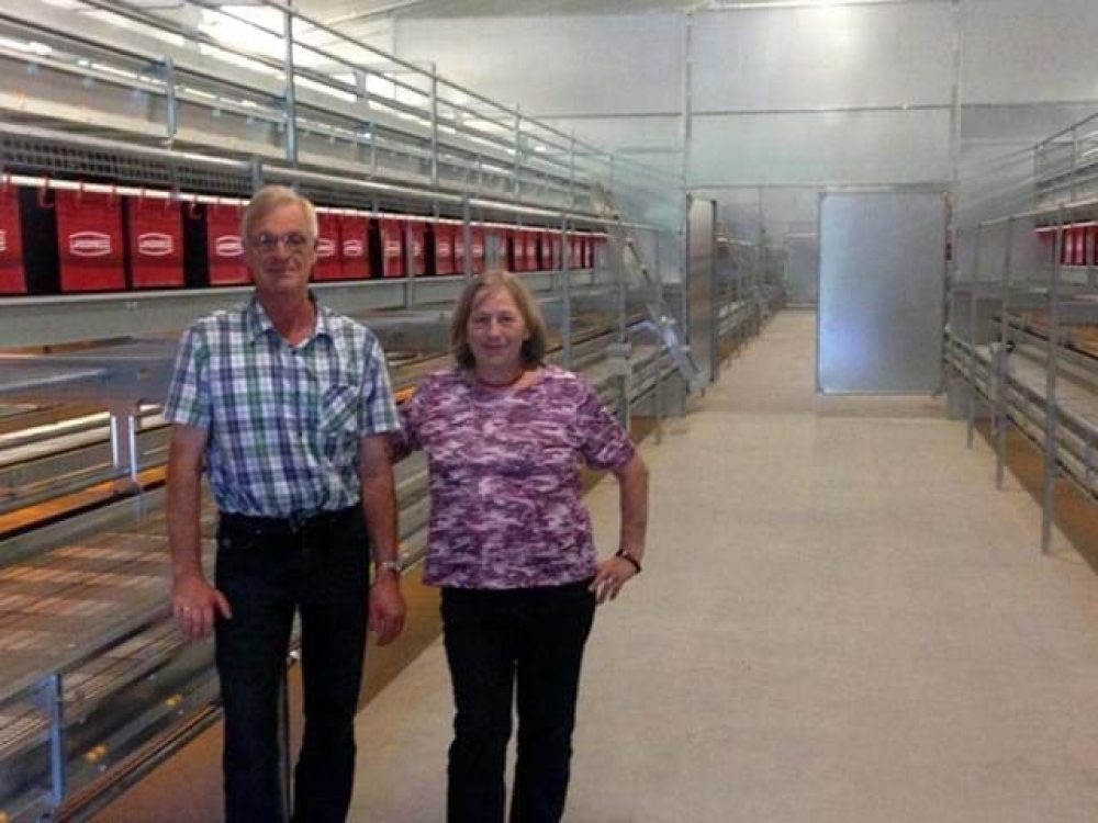 Man and woman in a poultry house with LANDMECO tiered aviary systems for cage-free egg production.