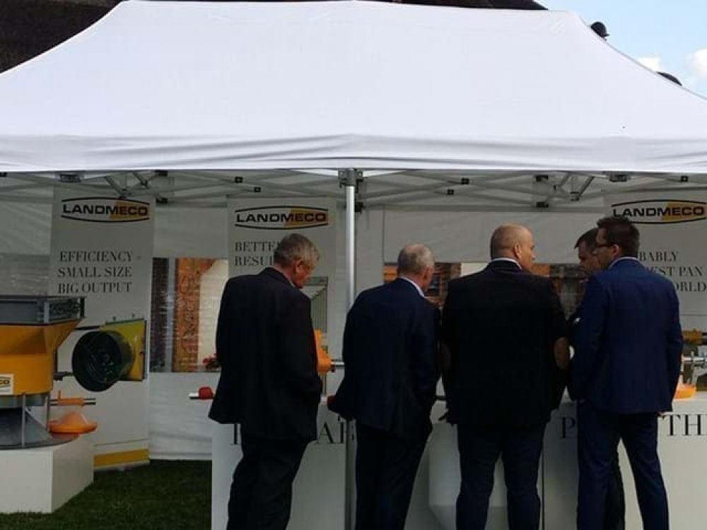 Professionals at a LANDMECO trade show booth inspecting automated poultry feeding systems and broiler equipment.