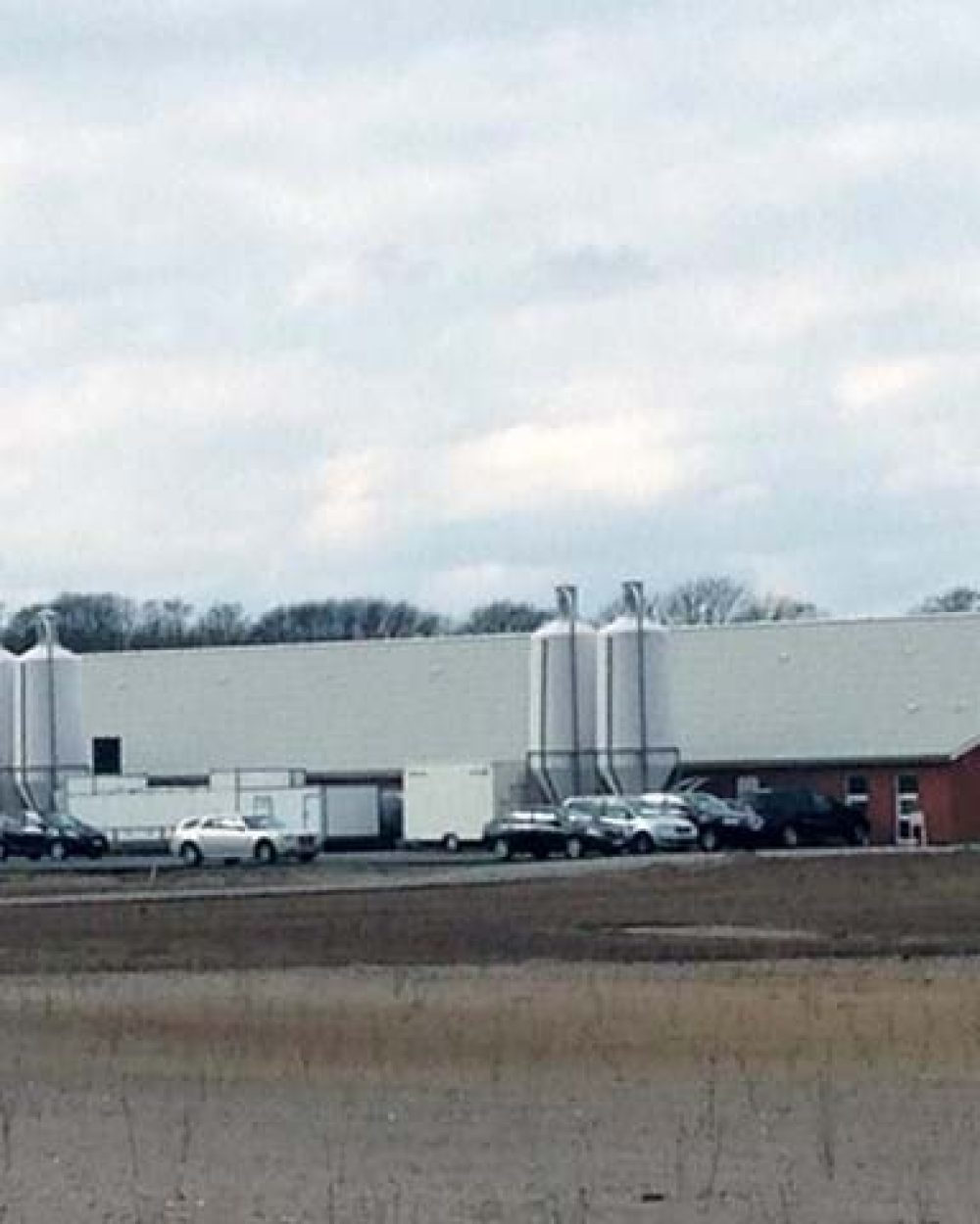 Industrial poultry house with white feed silos and office building, highlighting LANDMECO automated farming systems.