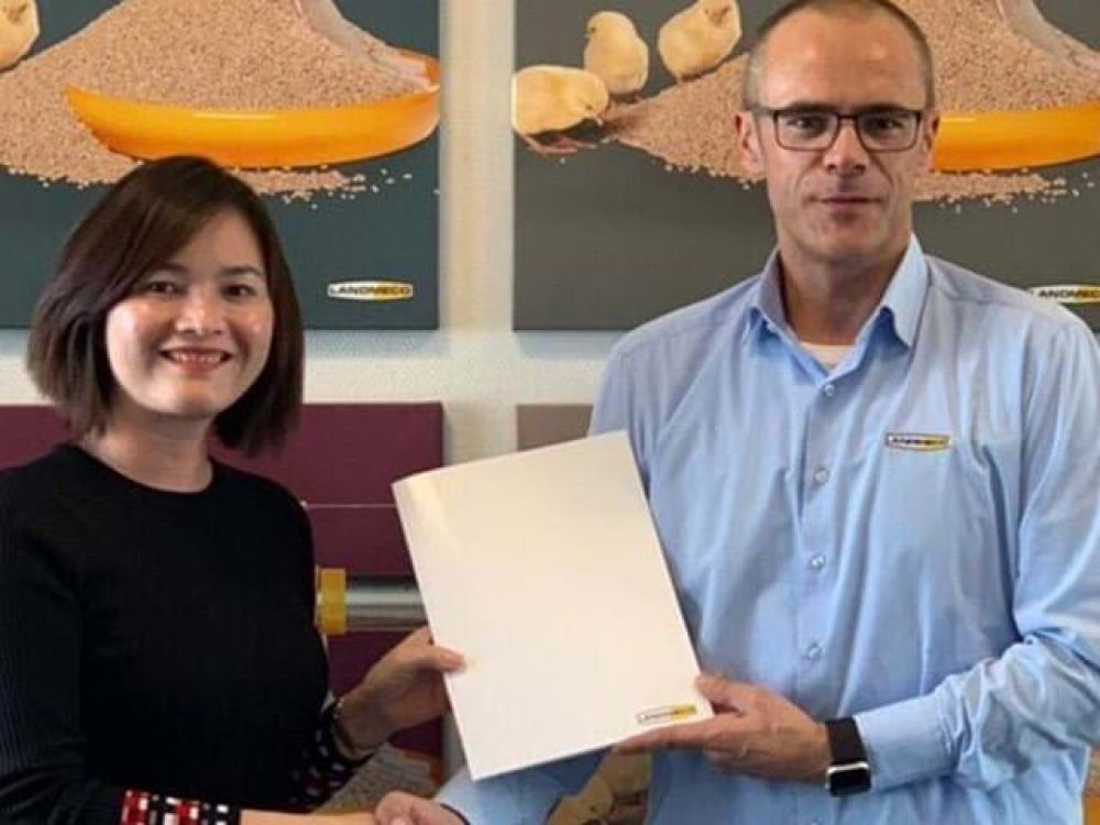 LANDMECO representatives hold a folder to celebrate the first order in Vietnam in front of poultry equipment posters.