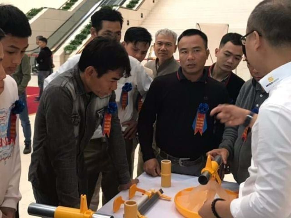 Professionals examining LANDMECO's Kick-off broiler pan feeding system at a poultry equipment demonstration.