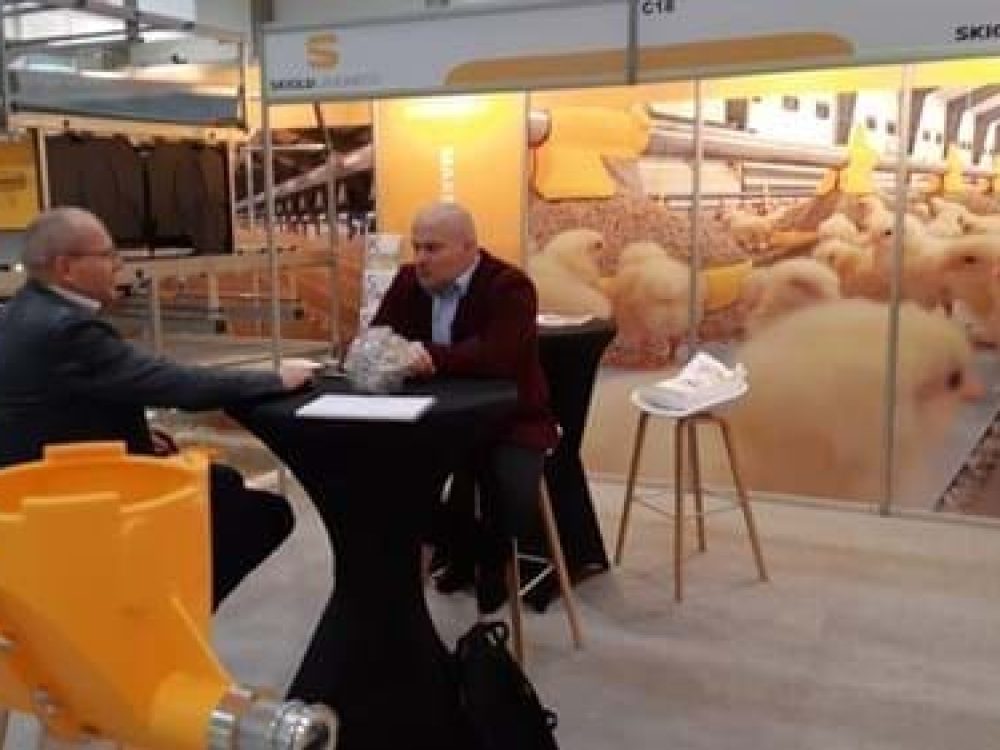 Professionals discussing poultry systems at a SKIOLD LANDMECO booth with a chick mural and feeding equipment.